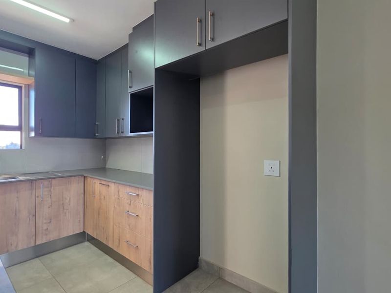 Modern kitchen featuring two-tone cabinetry, laminate countertops, integrated hob, and a dedicated refrigerator alcove with tiled flooring.