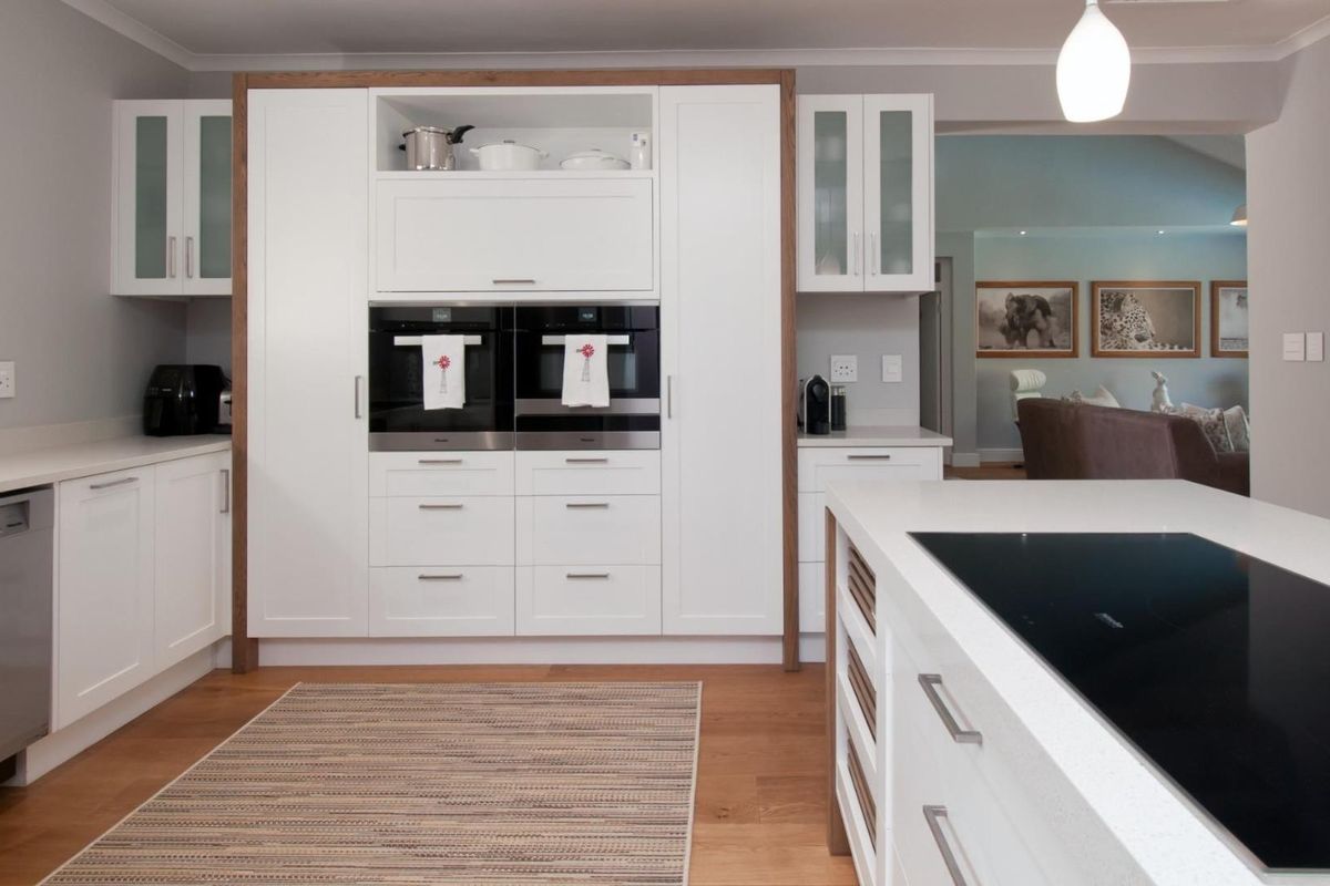 Modern kitchen featuring white cabinetry, integrated double ovens, a central island with a built-in induction cooktop, and high-quality timber flooring.