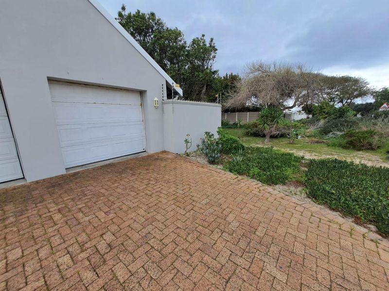 Exterior view of the cottage featuring a brick paved driveway, garage access, and perimeter wall with electric fencing.