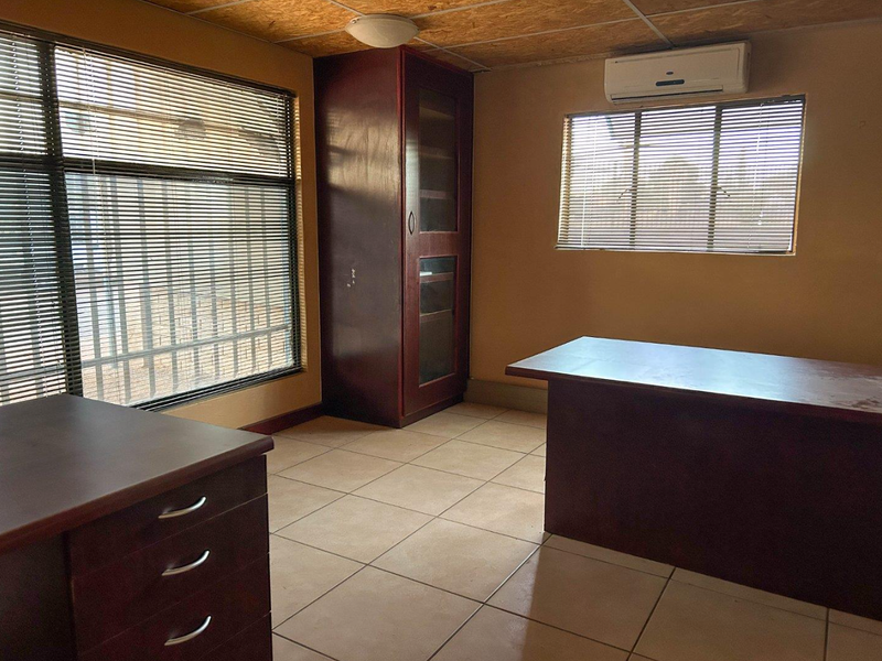 A functional office space featuring tiled flooring, a built-in storage cabinet, split-system air conditioning, and large windows with venetian blinds.