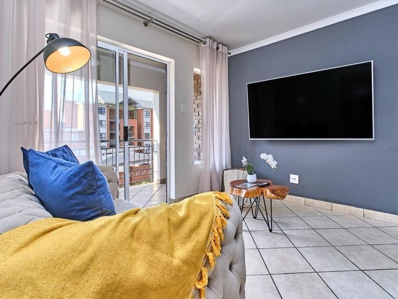 A bright living room featuring tiled flooring, a modern grey accent wall, and a sliding glass door providing access to a balcony.
