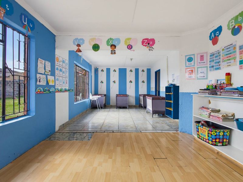 A multi-purpose room currently utilized as a daycare or classroom, featuring a mix of laminate and tiled flooring with security bars on windows.