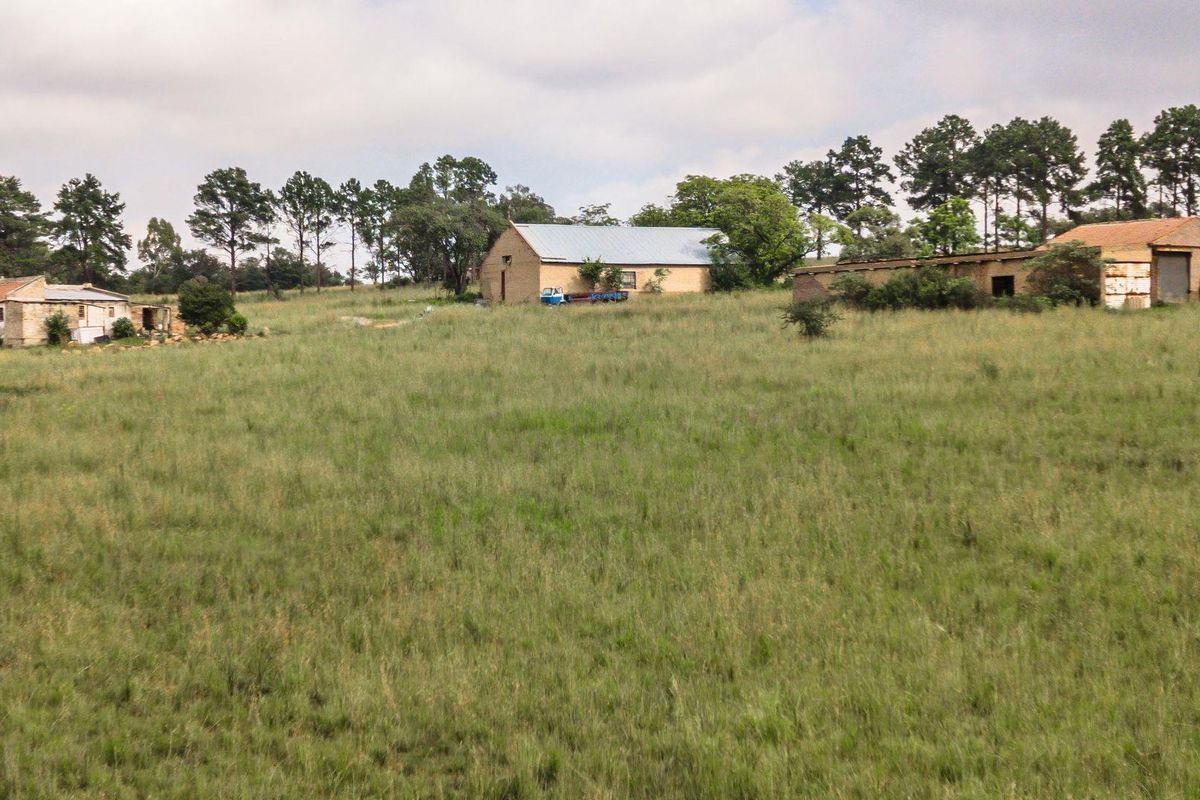 A wide-angle view of a rural farm property featuring multiple outbuildings and barns set within a large, open grassy field.
