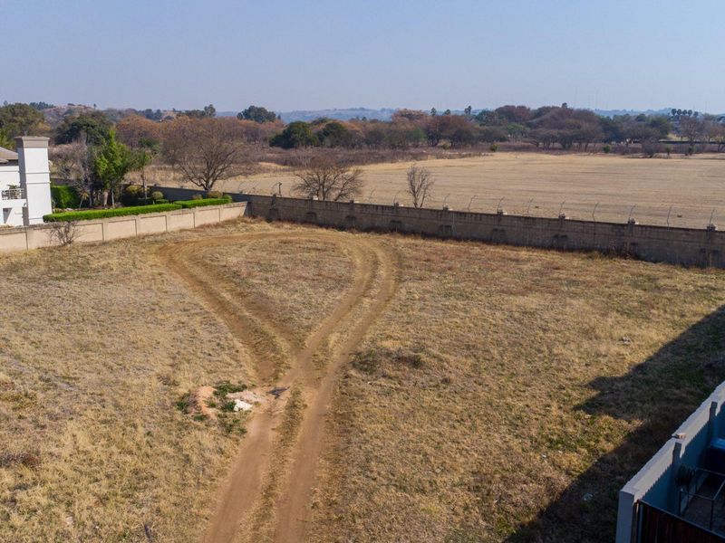 Aerial view of a vacant residential plot featuring a perimeter wall with electric fencing, offering a clear perspective of the land and surrounding area.