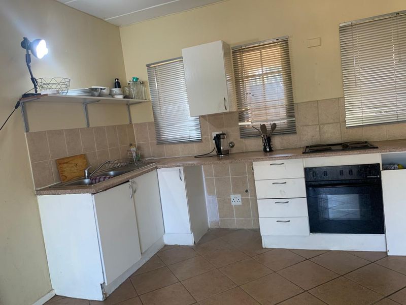 A functional kitchen featuring built-in cabinetry, a tiled backsplash, integrated oven and hob, and ceramic floor tiles, offering potential for cosmetic updates.