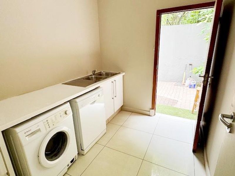 A functional laundry room featuring built-in cabinetry, a stainless steel sink, and direct access to an outdoor paved area.