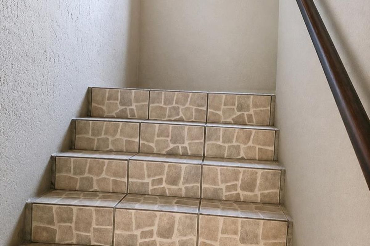 A functional indoor staircase featuring stone-look ceramic tiling and a mounted wooden handrail.