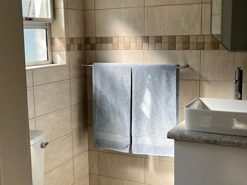 A functional bathroom featuring neutral wall and floor tiling, a modern vessel sink on a vanity cabinet, and a window for natural light.