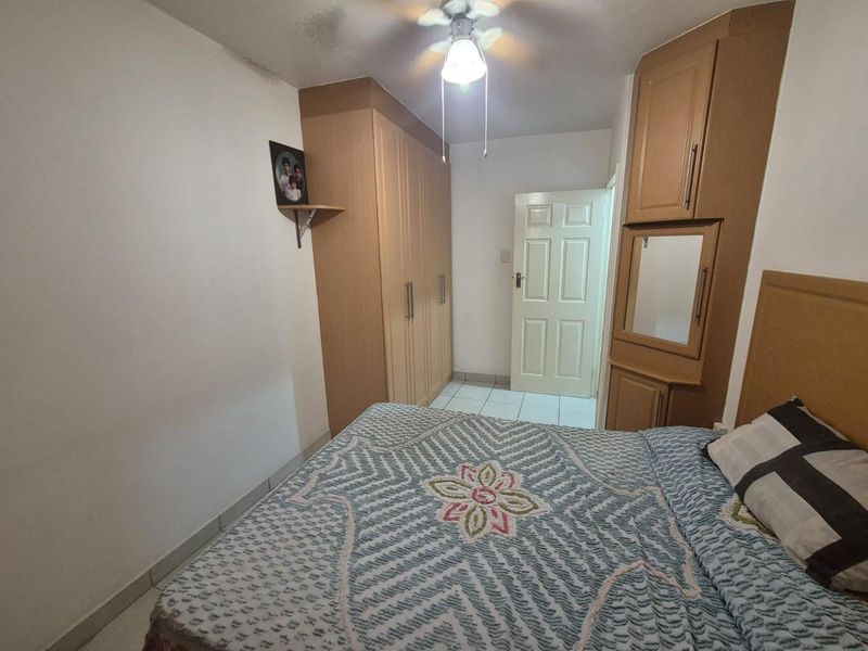 A bedroom featuring built-in wooden cupboards, tiled flooring, and a ceiling fan, providing functional storage and basic finishes.