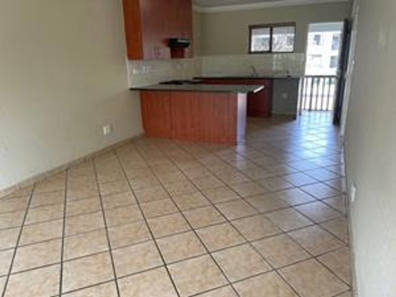An open-plan living and kitchen area featuring tiled flooring, built-in wooden cabinetry, and a kitchen island, leading to an outdoor balcony.