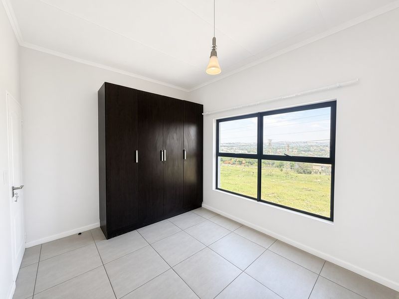 A bright, empty bedroom featuring neutral tiled flooring, a dark built-in wardrobe, and a large window offering scenic views.