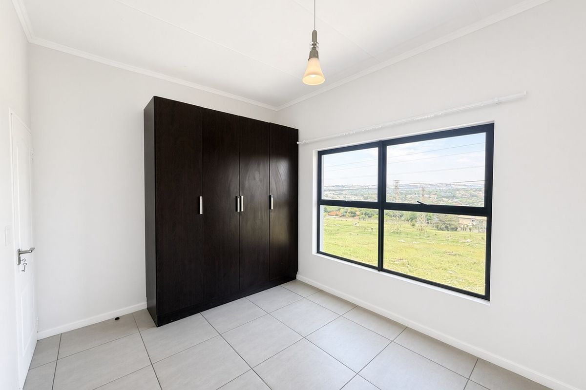 A bright, empty bedroom featuring neutral tiled flooring, a dark built-in wardrobe, and a large window offering scenic views.