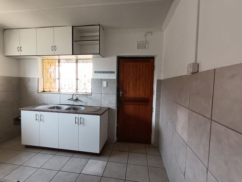 A functional kitchen space featuring built-in cabinetry, a stainless steel sink, tiled splashbacks, and tiled flooring, offering a blank canvas for renovation.