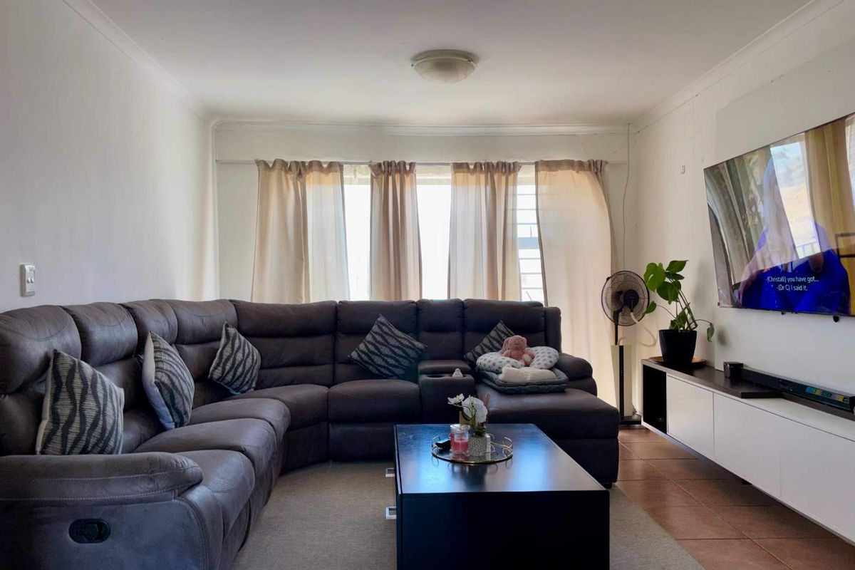 A comfortable living room featuring tiled flooring, large windows with natural light, and a wall-mounted television setup.