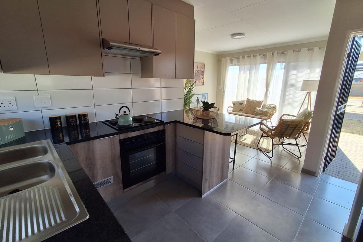 Modern open-plan kitchen featuring granite countertops, built-in oven, and hob, flowing seamlessly into a bright living area with large sliding doors.