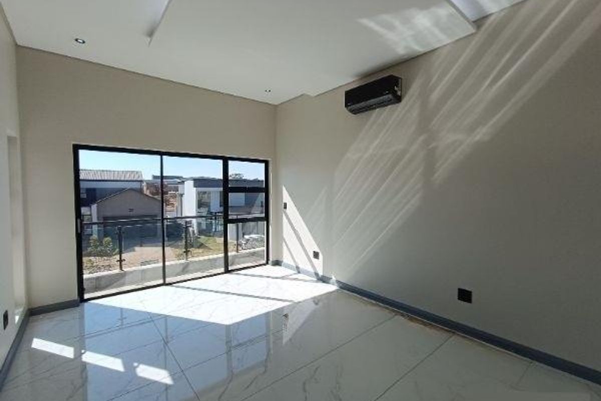 A bright, empty bedroom featuring modern porcelain tile flooring, a recessed ceiling, and a large sliding glass door leading to a balcony.