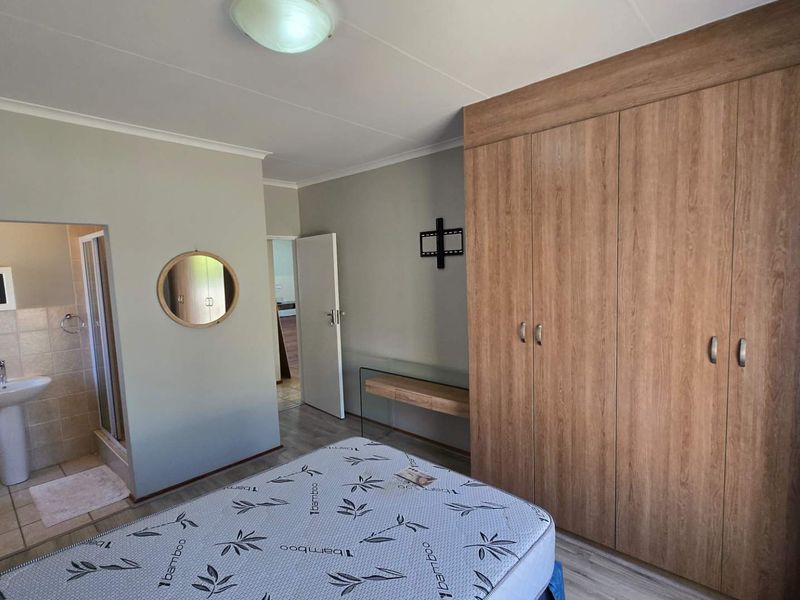 A well-maintained bedroom featuring built-in wooden wardrobes and an attached en-suite bathroom with a pedestal basin and shower.