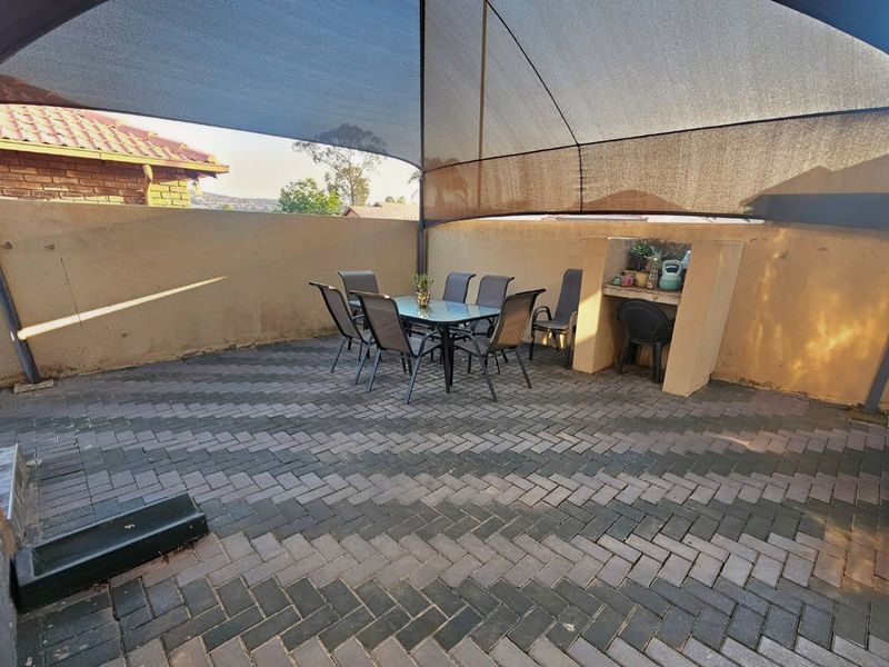 Outdoor patio area featuring herringbone paving, a built-in braai station, and a large overhead shade sail for sun protection.