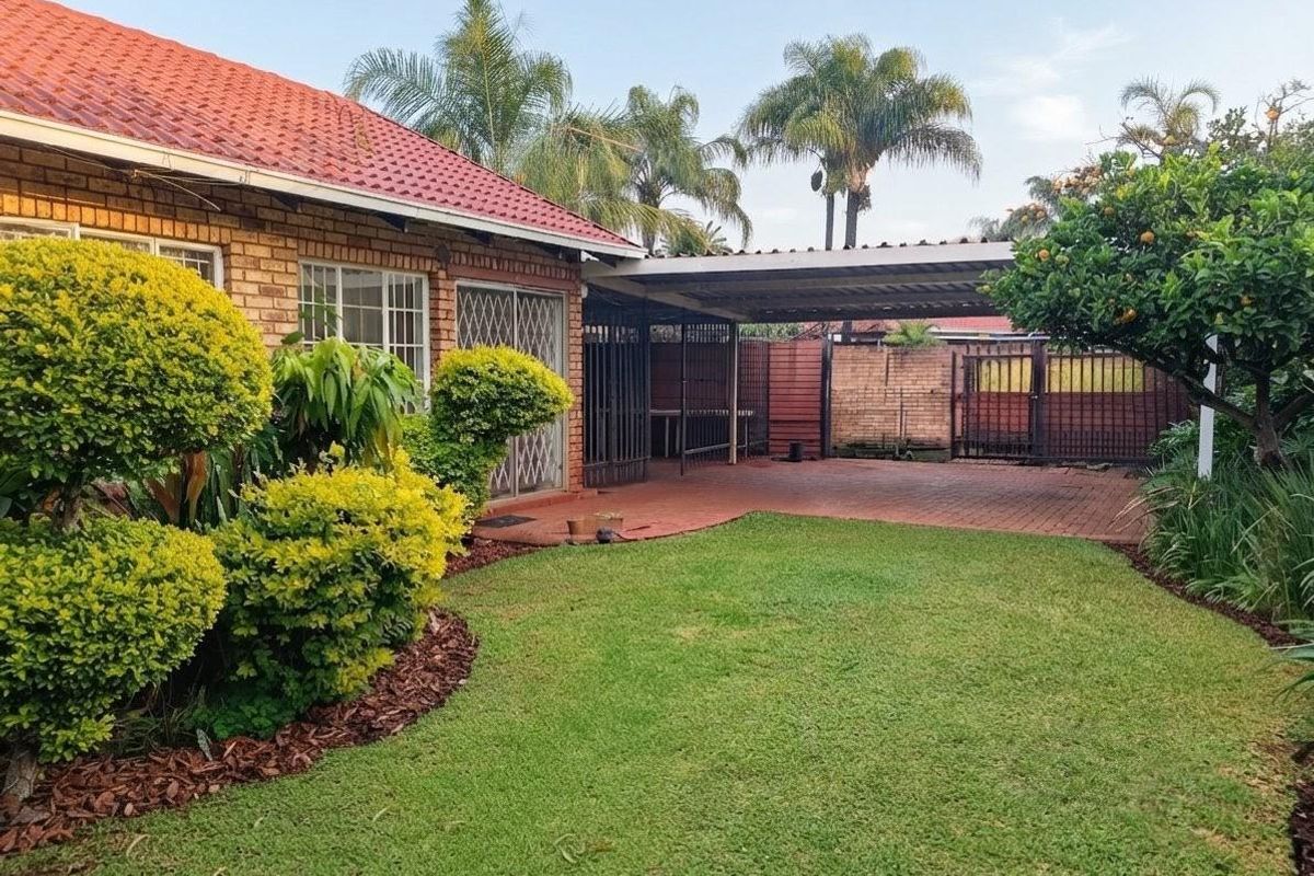 Rear view of the townhouse featuring a paved driveway, covered carport, brick exterior, and a well-maintained garden area.