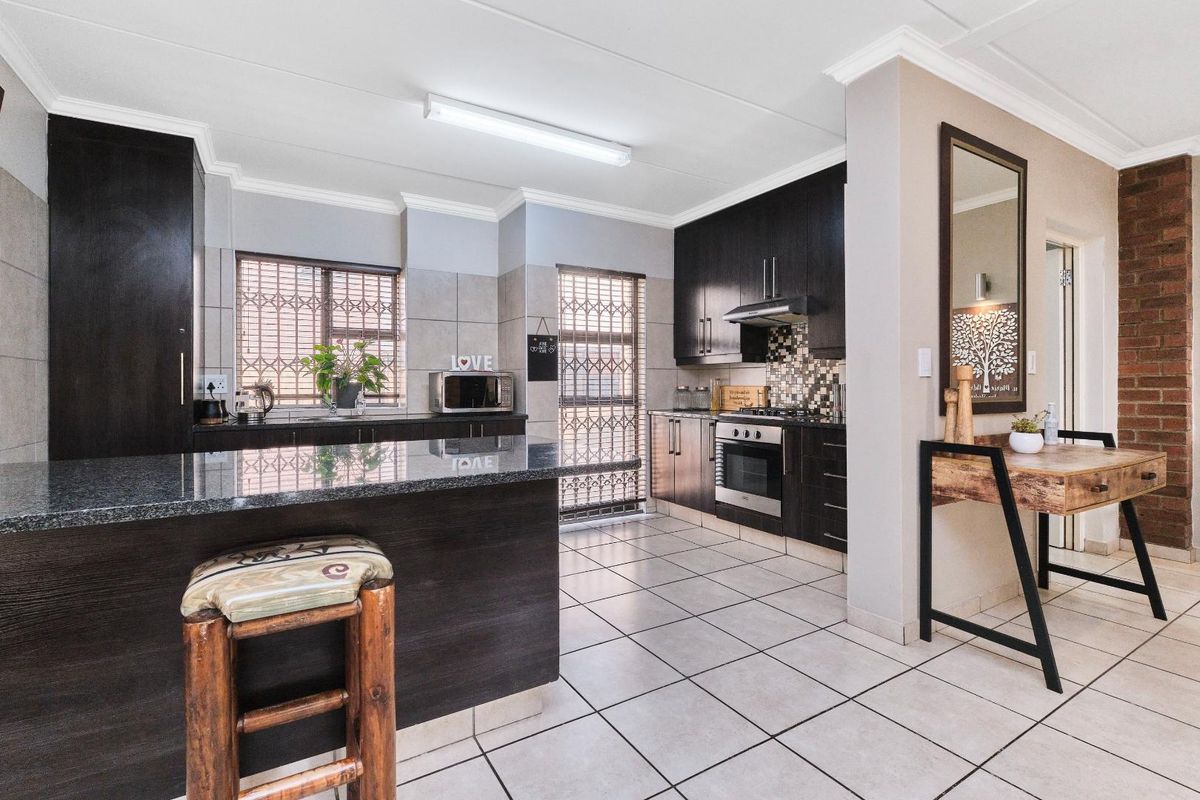 A functional kitchen featuring dark cabinetry, granite countertops, a built-in oven and hob, and tiled flooring with a breakfast nook.