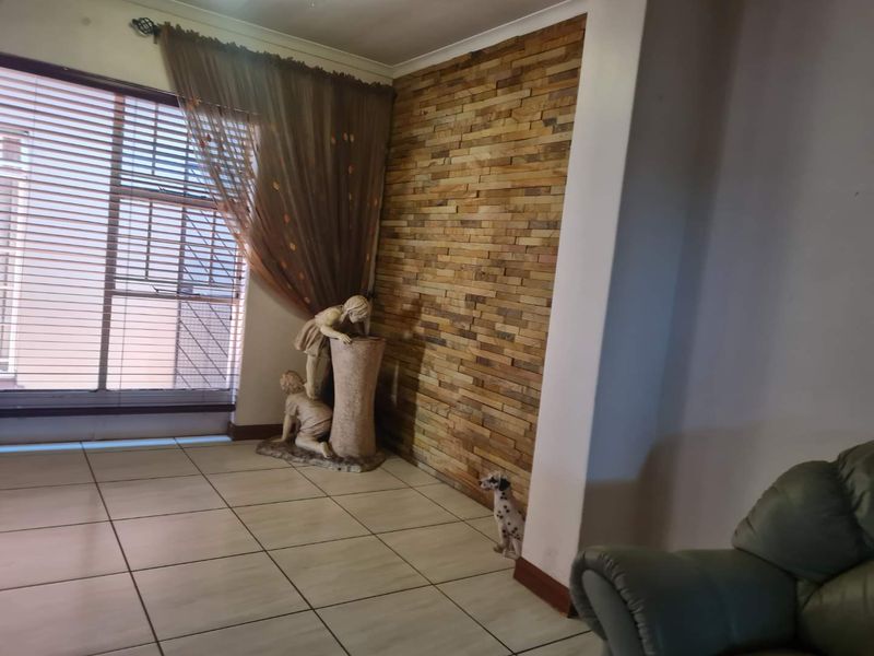 Living room area featuring a textured stone veneer accent wall, neutral ceramic floor tiles, and large window with fitted venetian blinds.