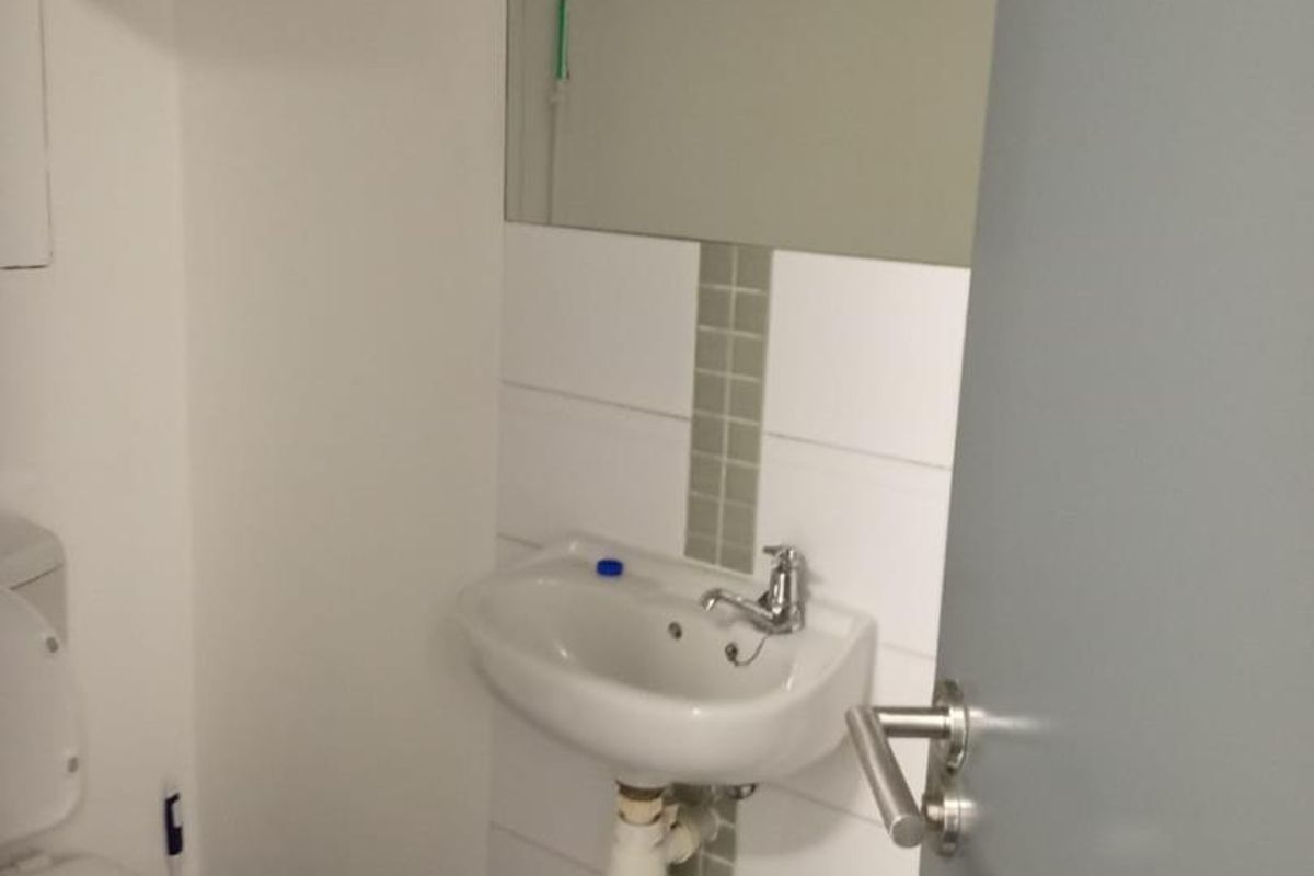 A functional industrial-style bathroom featuring a wall-mounted basin with chrome faucet, tiled splashback, wall mirror, and a standard toilet.