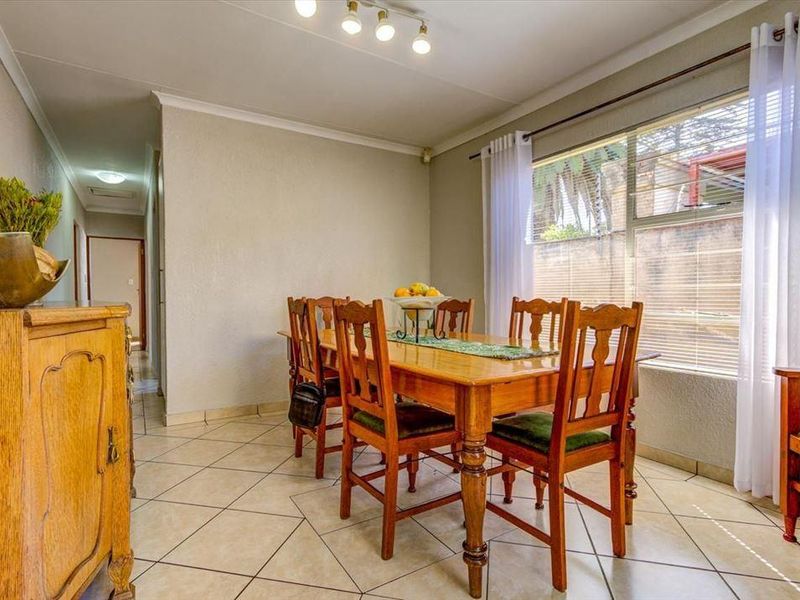 A well-lit dining room featuring neutral wall finishes, tiled flooring, and a large window allowing for natural light.