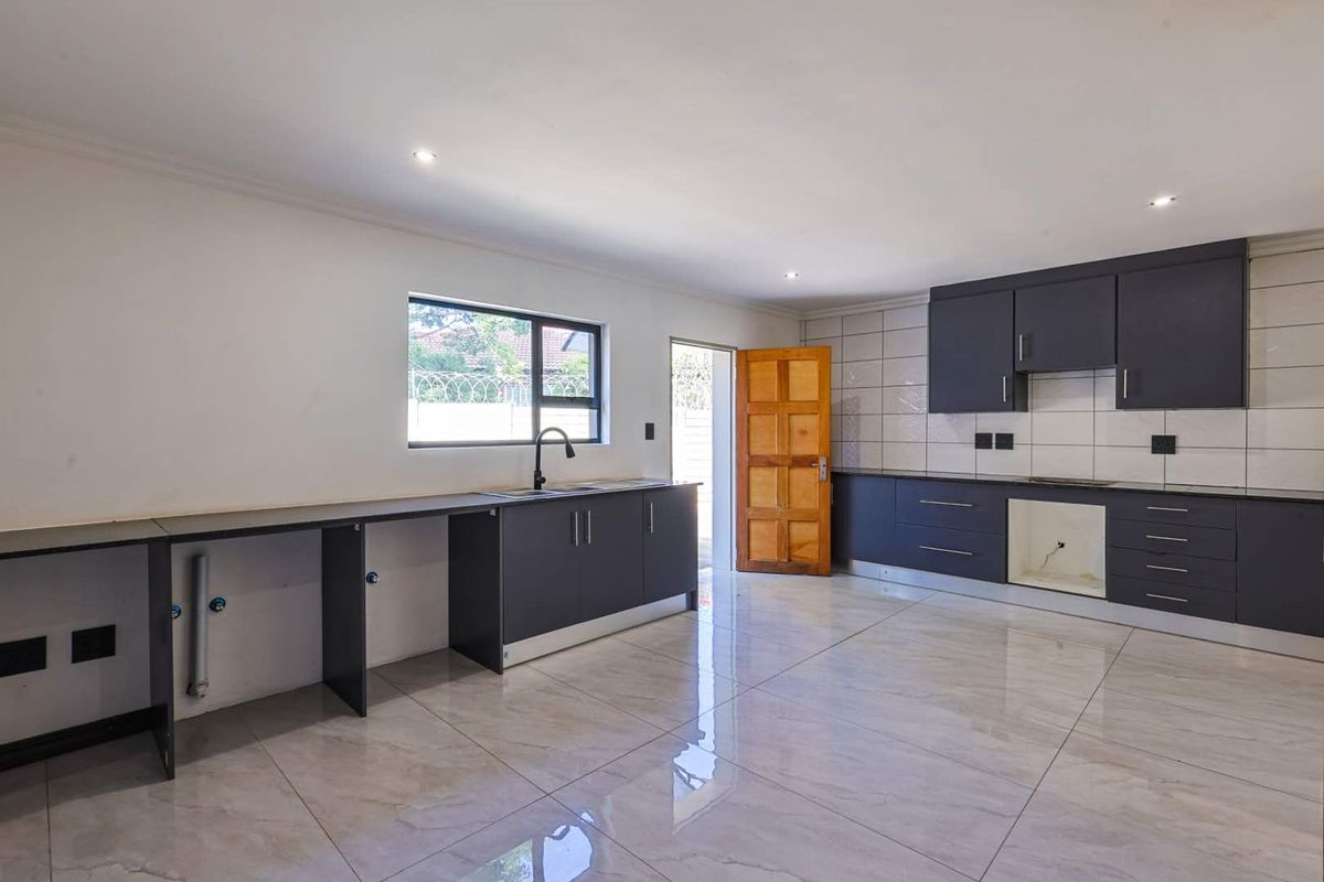 Modern kitchen featuring dark grey cabinetry, tiled flooring, and a large window, providing a clean and functional space ready for final appliance installation.