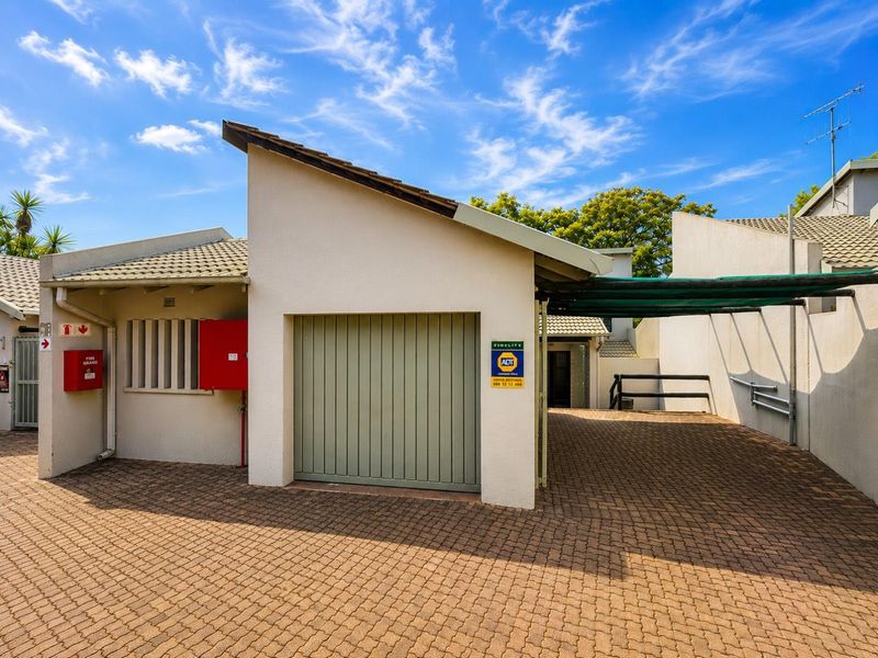 Exterior view of a residential garage featuring a paved driveway, integrated fire safety equipment, and a covered parking area with shade cloth.