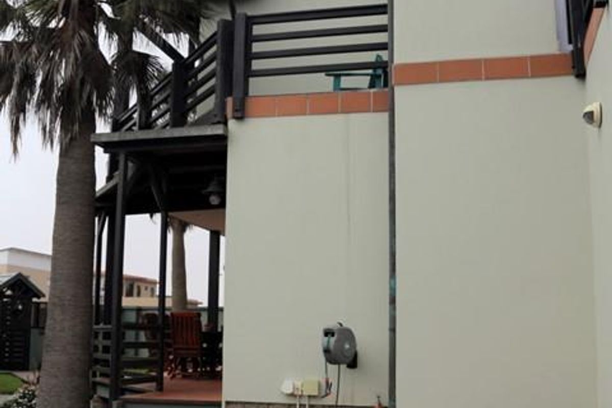 Rear exterior view of the property featuring a brick paved area, stone cladding base, and a raised timber balcony with tiled steps.