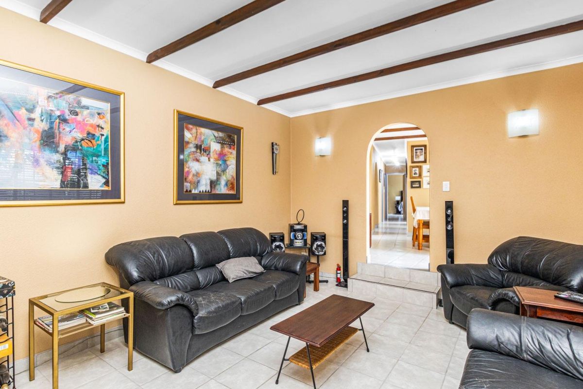 A living room featuring exposed timber ceiling beams, tiled flooring, and an arched doorway leading to an adjacent space.