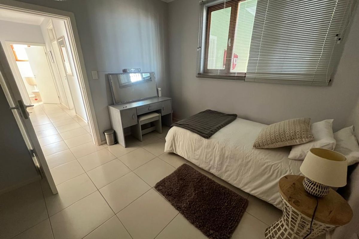 A bedroom featuring tiled flooring, a window with fitted blinds, and direct access to an adjacent hallway and bathroom.