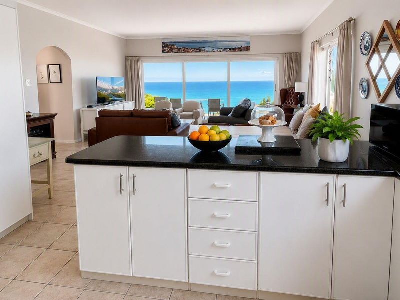 Spacious open-plan living area featuring a modern kitchen island with granite countertops, flowing seamlessly into a bright lounge with stunning ocean views.