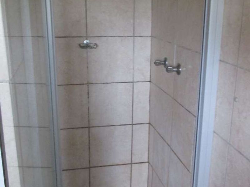 A compact shower stall featuring tiled walls and flooring with a glass enclosure, requiring maintenance to address grout and surface cleanliness.