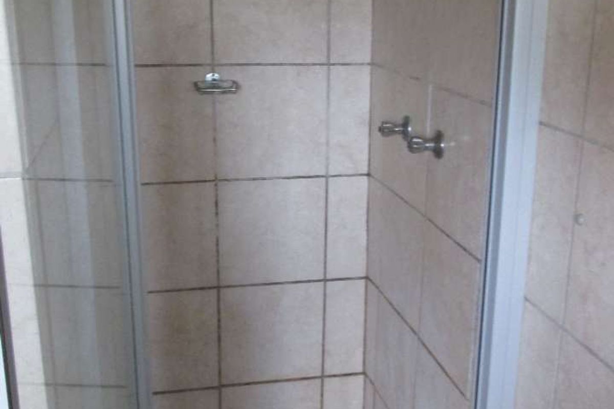 A compact shower stall featuring tiled walls and flooring with a glass enclosure, requiring maintenance to address grout and surface cleanliness.