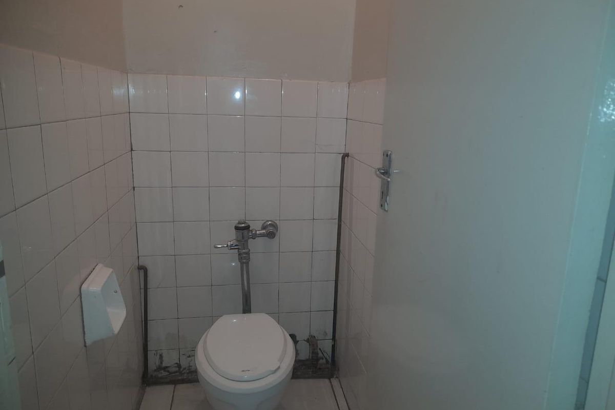 A compact bathroom featuring a flush toilet, white wall tiling, and exposed plumbing fixtures.