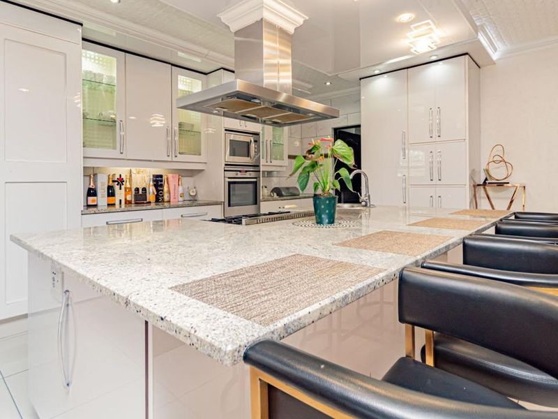 Modern kitchen featuring a large granite island, high-gloss cabinetry, built-in stainless steel appliances, and elegant ceiling detailing.