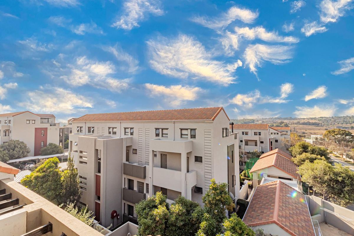 An elevated aerial view of a modern apartment complex featuring tiled roofs, neutral facade finishes, and surrounding landscaped greenery.