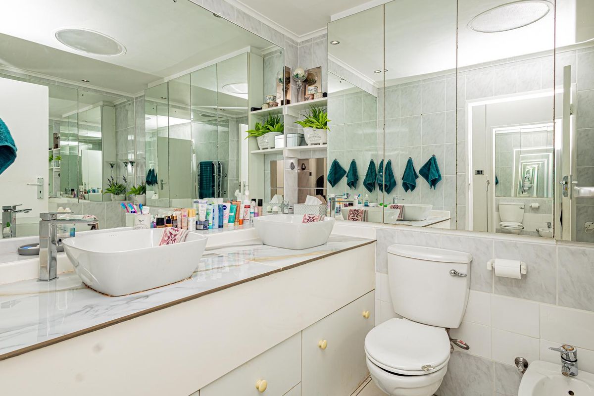 A functional bathroom featuring a double vanity with vessel sinks, extensive wall-to-wall mirrors, built-in shelving, a toilet, and a bidet with tiled finishes.