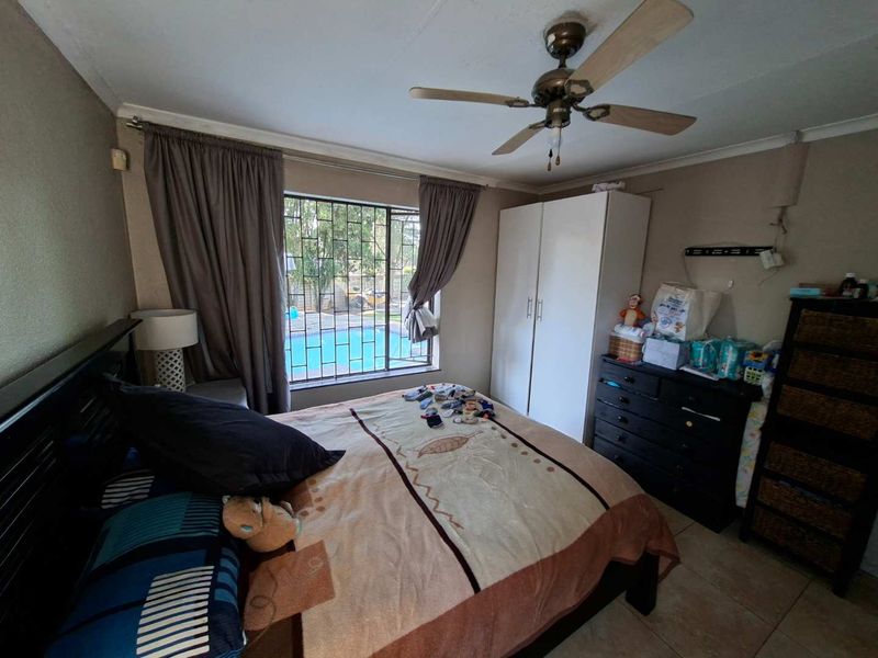 A functional bedroom featuring a ceiling fan, built-in wardrobe, and tiled flooring, with a view overlooking the pool area.