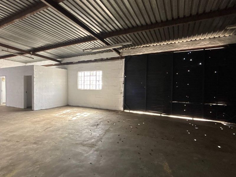Spacious industrial utility area featuring exposed steel roof trusses, concrete flooring, and a large sliding access door with natural light entry.