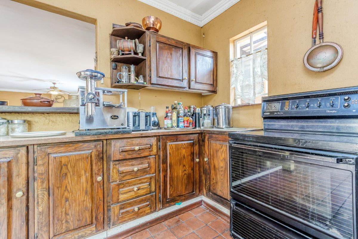 A dated kitchen featuring traditional dark wood cabinetry, a built-in oven, and terracotta floor tiles, offering a classic layout with potential for modernization.