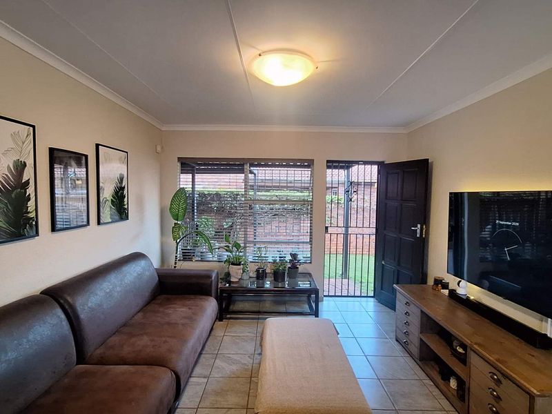 A comfortable living room featuring tiled flooring, a security gate leading to the exterior, and a window with security bars.