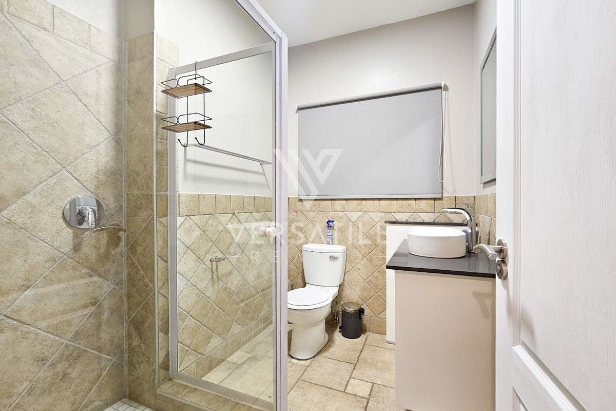 A well-maintained bathroom featuring a glass-enclosed shower, stone-tiled walls and flooring, a modern vessel sink vanity, and a neutral color palette.