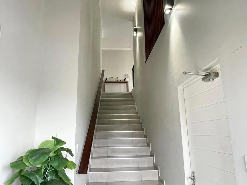 A bright, modern hallway featuring a tiled staircase with a wooden handrail and contemporary wall-mounted lighting.