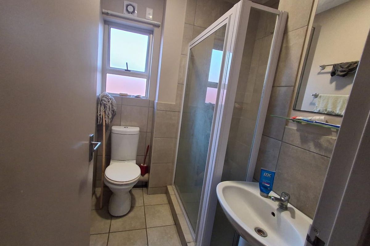 A functional bathroom featuring a glass-enclosed shower, pedestal basin, and toilet with neutral wall and floor tiling.