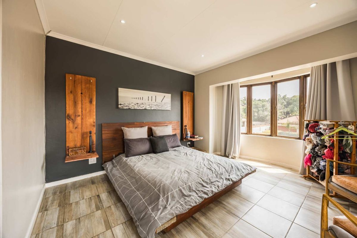 A well-lit bedroom featuring tiled flooring, a dark accent wall, and a large window providing natural light.