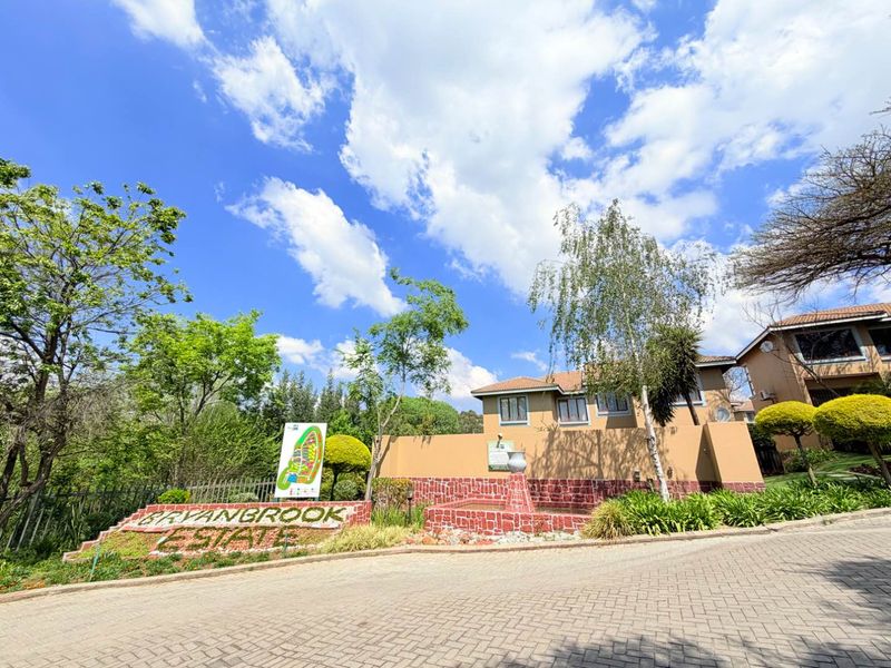 The entrance to Bryanbrook Estate featuring a paved driveway, stone-clad boundary wall, and well-maintained landscaped gardens.