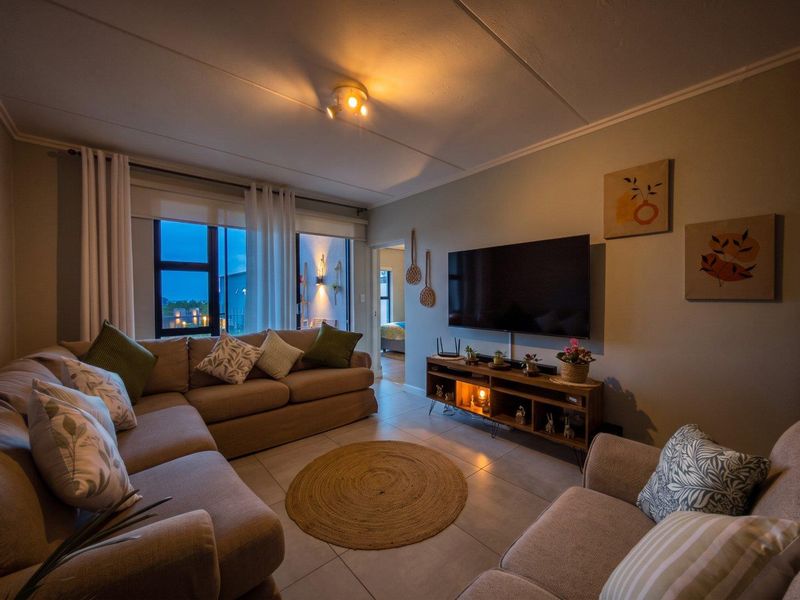 A cozy living room featuring tiled flooring, neutral wall tones, and a sliding glass door providing access to an outdoor balcony area.