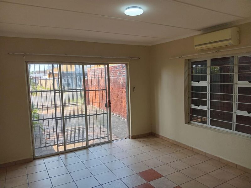 An empty living room featuring tiled flooring, a sliding glass door with security bars, and a wall-mounted air conditioning unit.